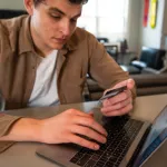 Person holding a payment card while paying a bill on a laptop