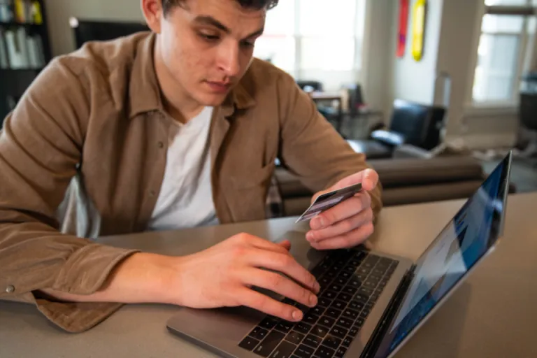 Person holding a payment card while paying a bill on a laptop