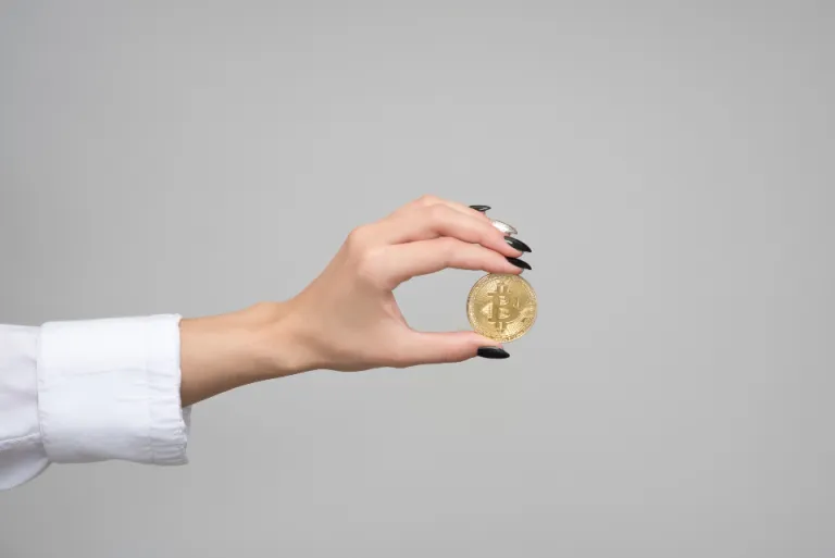 Hand holding a gold-coloured bitcoin coin against a plain grey background