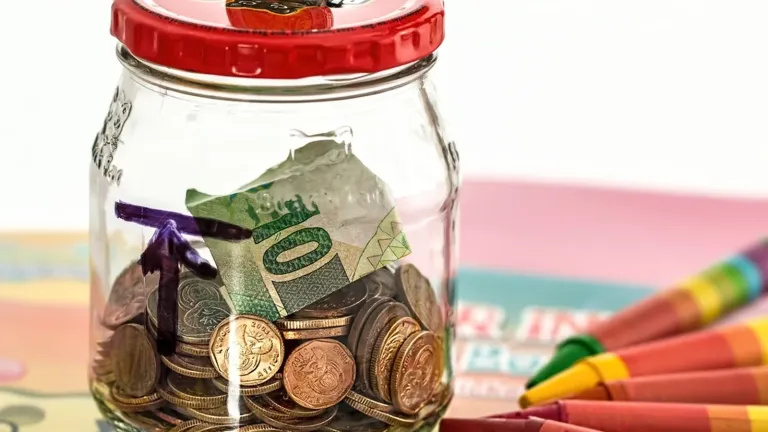 Glass savings jar labeled emergency fund on a kitchen table