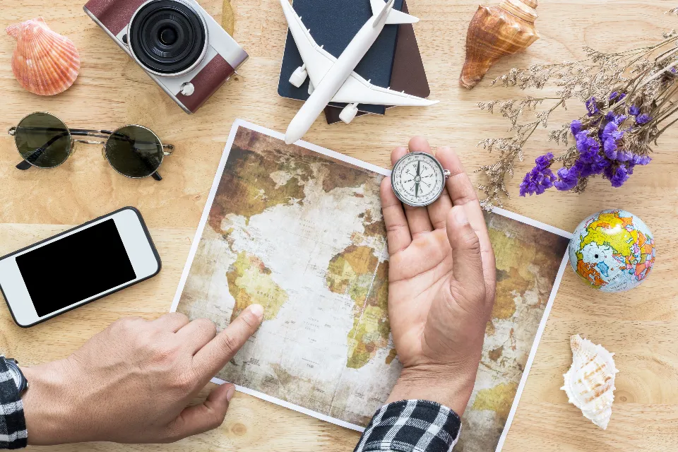 Hands planning a trip on a world map surrounded by travel essentials