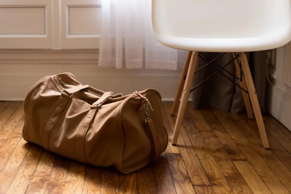 Single brown duffel bag packed for a trip on a wooden floor