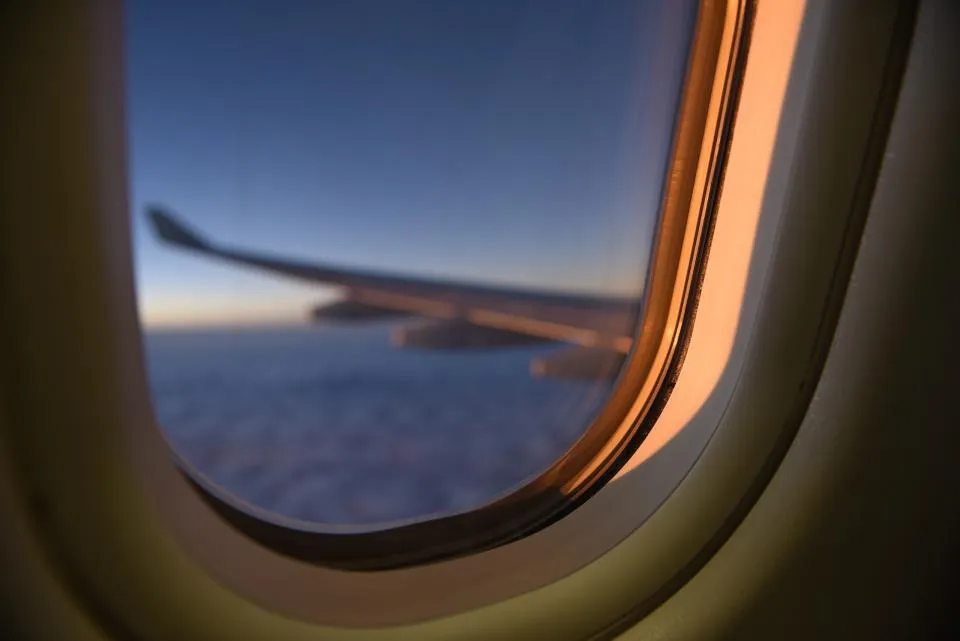 Airplane wing at dusk seen through a cabin window on a long-haul flight
