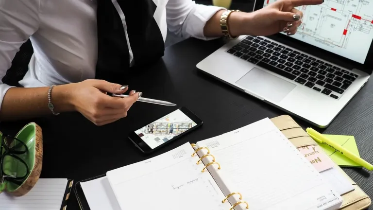 Hands writing a one-page business plan in a notebook next to a laptop