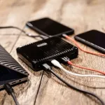 Two smartphones charging from a power bank on a wooden table
