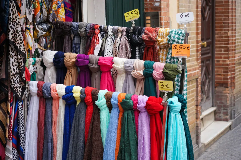 Colorful scarves with handwritten price tags on a rack outside a small shop