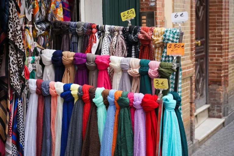 Colorful scarves with handwritten price tags on a rack outside a small shop